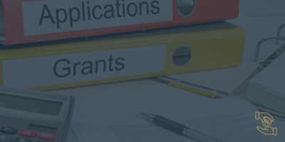 There is a yellow folder with an orange folder on top. They have writing on them grants and applications. They are there to symbolise grant funding