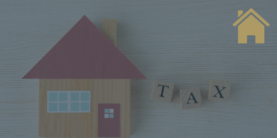 a picture of a house with a red roof and a red door. The word tax is written on scrabble tiles next to the house. there is a small gold house symbol in the top right hand corner of the picture.